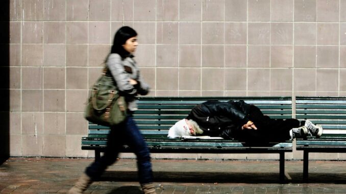 Woman walks past person sleeping on bench. Woman walks past person sleeping on bench.