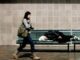 Woman walks past person sleeping on bench.