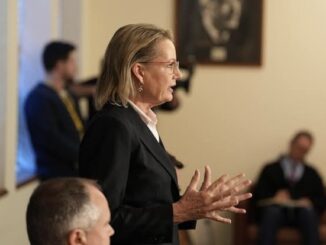 Woman speaking in a formal meeting setting.