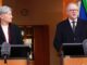 Two speakers at podiums with microphones and flag