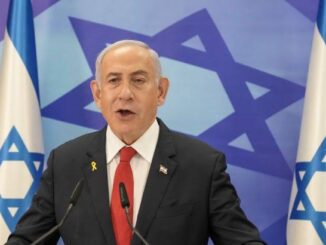 Man speaking in front of Israeli flags.