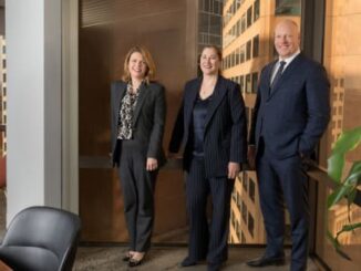 Three professionals standing in office setting.
