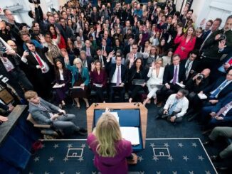 Press conference with seated audience and speaker.