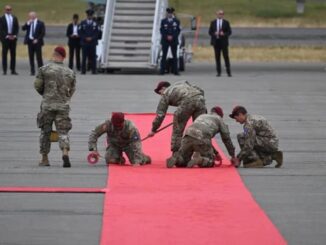 Soldiers preparing red carpet on airport runway.