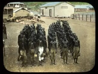 Men standing in chains outside industrial buildings.