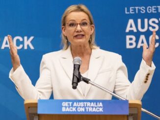 Woman speaking at podium with raised hands.