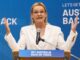 Woman speaking at podium with raised hands.
