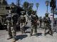 Armed soldiers in tactical gear on street.