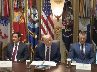 Five officials seated beneath flags at table