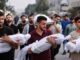 Men carrying wrapped bodies in a procession.