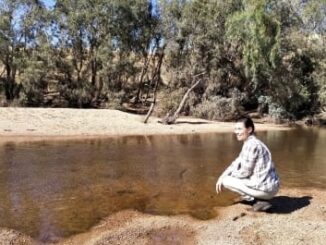 Person squatting by a tranquil riverside.