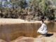 Person squatting by a tranquil riverside.