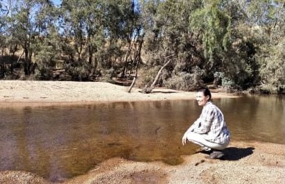 Person squatting by a tranquil riverside.