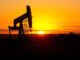 Oil pumpjack silhouette against sunset sky.