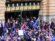 Crowd with flags outside building entrance.