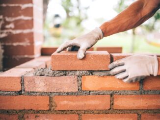 Bricklayer placing bricks on mortar wall.