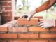 Bricklayer placing bricks on mortar wall.