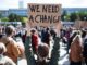 Person holding "We Need A Change" sign.