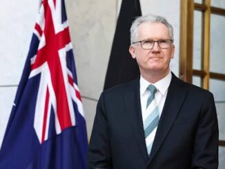 Man in suit standing by Australian flag.