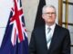 Man in suit standing by Australian flag.