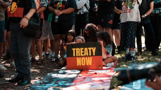 People gathered holding a "Treaty Now" sign.