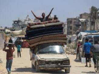 Man on car with stacked mattresses, cheering.