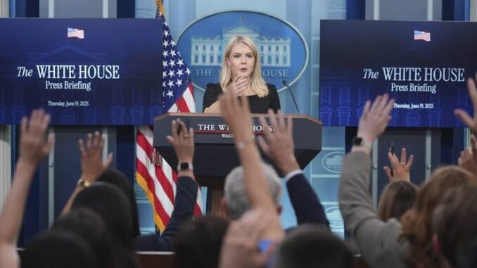 Press briefing with speaker, audience raising hands.