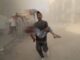 Man carrying injured child through dusty street.