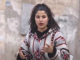 Woman speaking outdoors in patterned jacket.