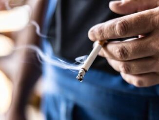 Thumb and forefinger clasp lit cigarette