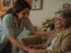 Caregiver assisting elderly woman in living room.