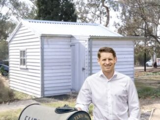 Man smiling in front of white shed.