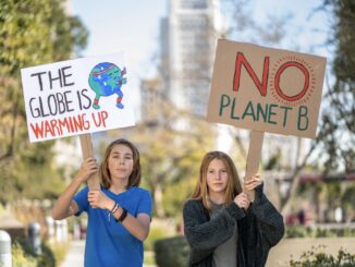 Teens holding climate change protest signs outdoors.
