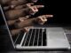 Hands pointing out of a laptop screen.