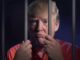Person behind bars wearing an orange shirt.