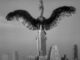 Giant bird atop skyscraper in black-and-white.