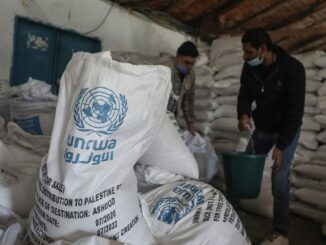 Men handling UNRWA aid sacks in warehouse.