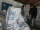 Men handling UNRWA aid sacks in warehouse.