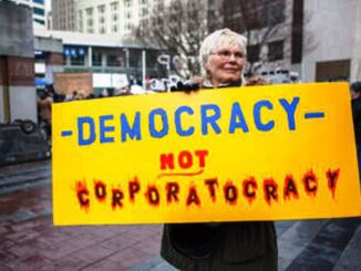 Protester holding "Democracy Not Corporatocracy" sign.