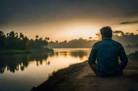 Man sitting by a river at sunset.