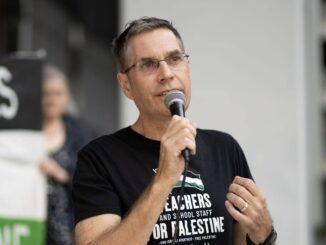 Man speaking into microphone, wearing black shirt.