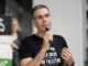 Man speaking into microphone, wearing black shirt.