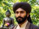 Man in turban with Buddha statue background.