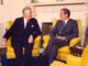 Two men seated in yellow chairs, conversing.