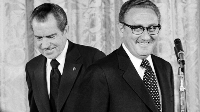 Two men in suits, one behind microphone. Two men in suits, one behind microphone.