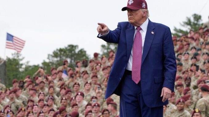 Man in suit pointing, addressing military audience.