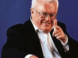 Man in suit smiling and pointing finger.