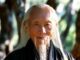 Elderly man with long white hair outdoors.