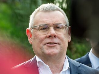 Man speaking outdoors, wearing glasses and suit.