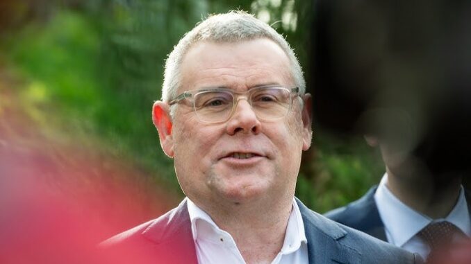 Man speaking outdoors, wearing glasses and suit.